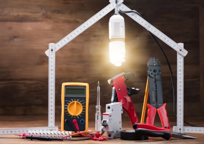 Blog del electricista en Málaga Herramientas de electricidad y bombilla encendida bajo una regla con forma de casa · Blog del electricista en Málaga